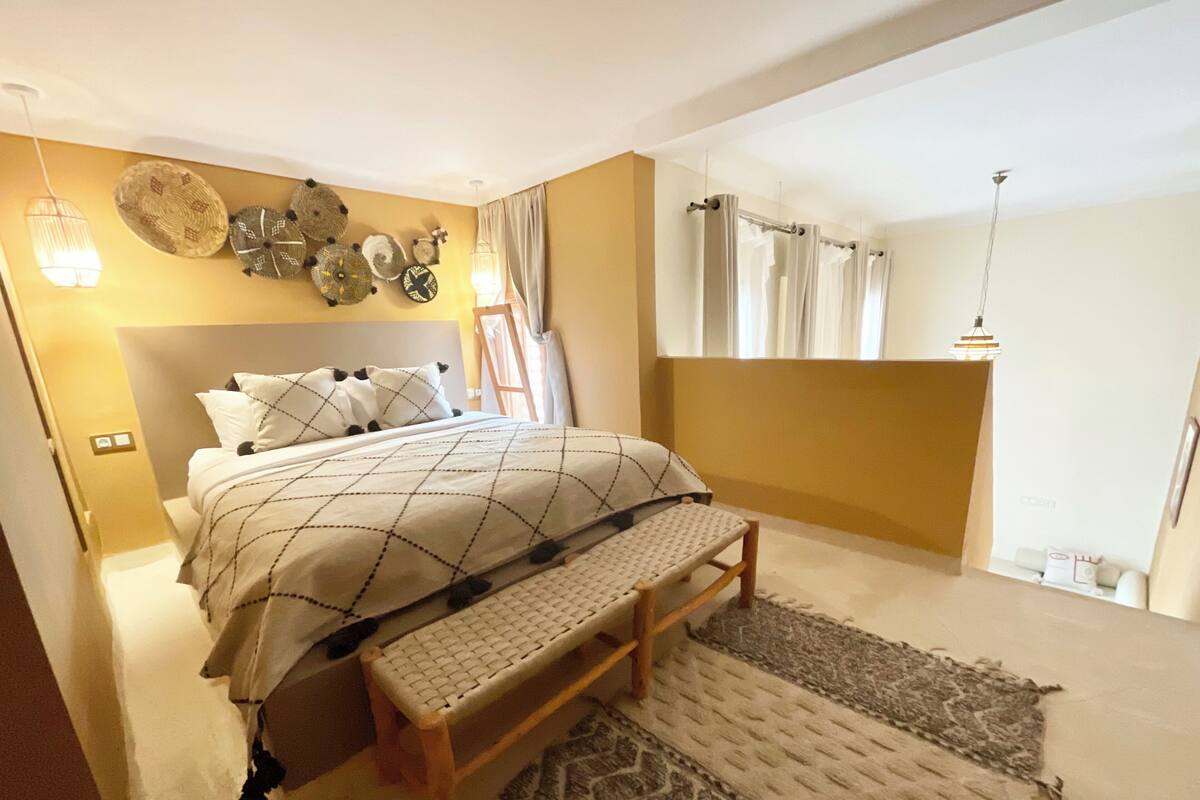 A bedroom with a bed, bench, wall decor, and a window with curtains.