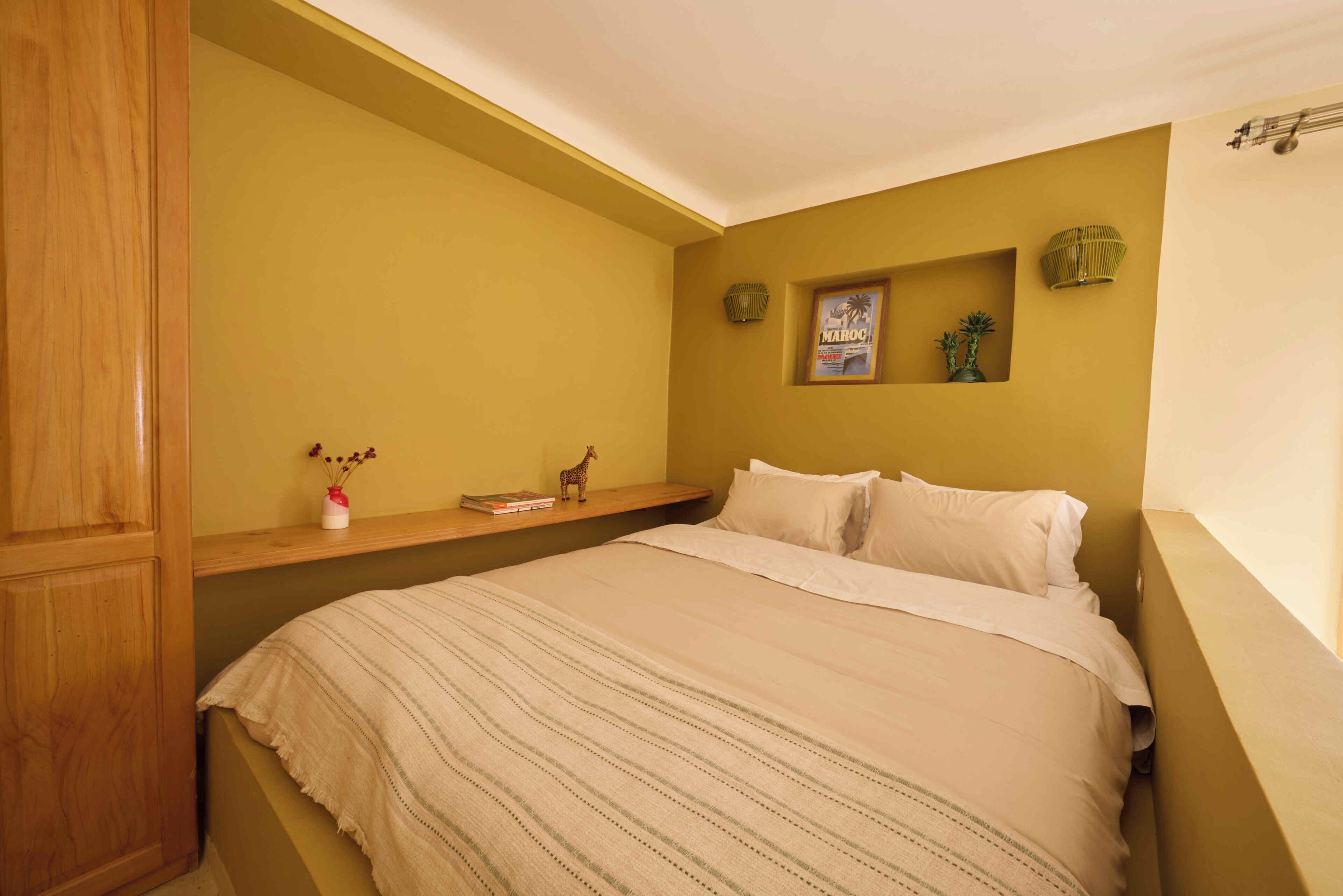 A bedroom with a bed, a shelf with books and a vase, a wall clock, and a framed picture.