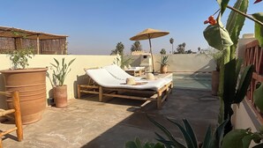 A rooftop lounge area with wooden lounge chairs, a table, and potted plants. - Riad Al Muhandiz (Marrakech)
