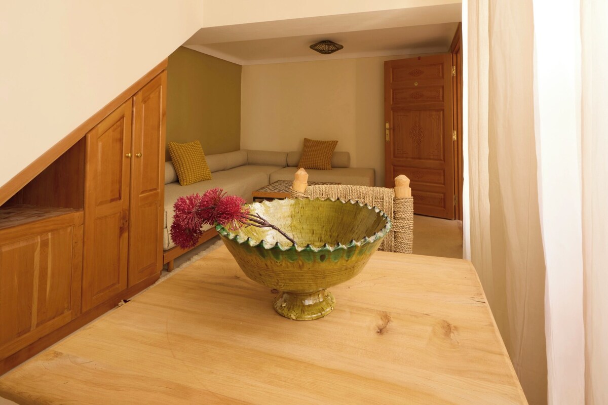 A room with a wooden table, a green decorative bowl, and a sofa with cushions.