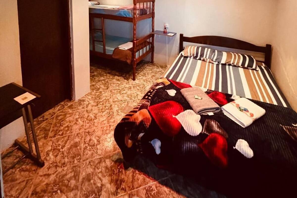A bedroom with a bunk bed, a bedside table, a chair, and a patterned carpet.