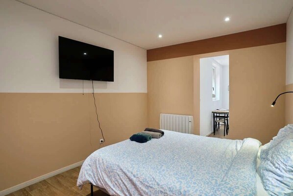 Une chambre à coucher comprenant un lit, un téléviseur fixé au mur, un radiateur et une petite table avec des chaises.