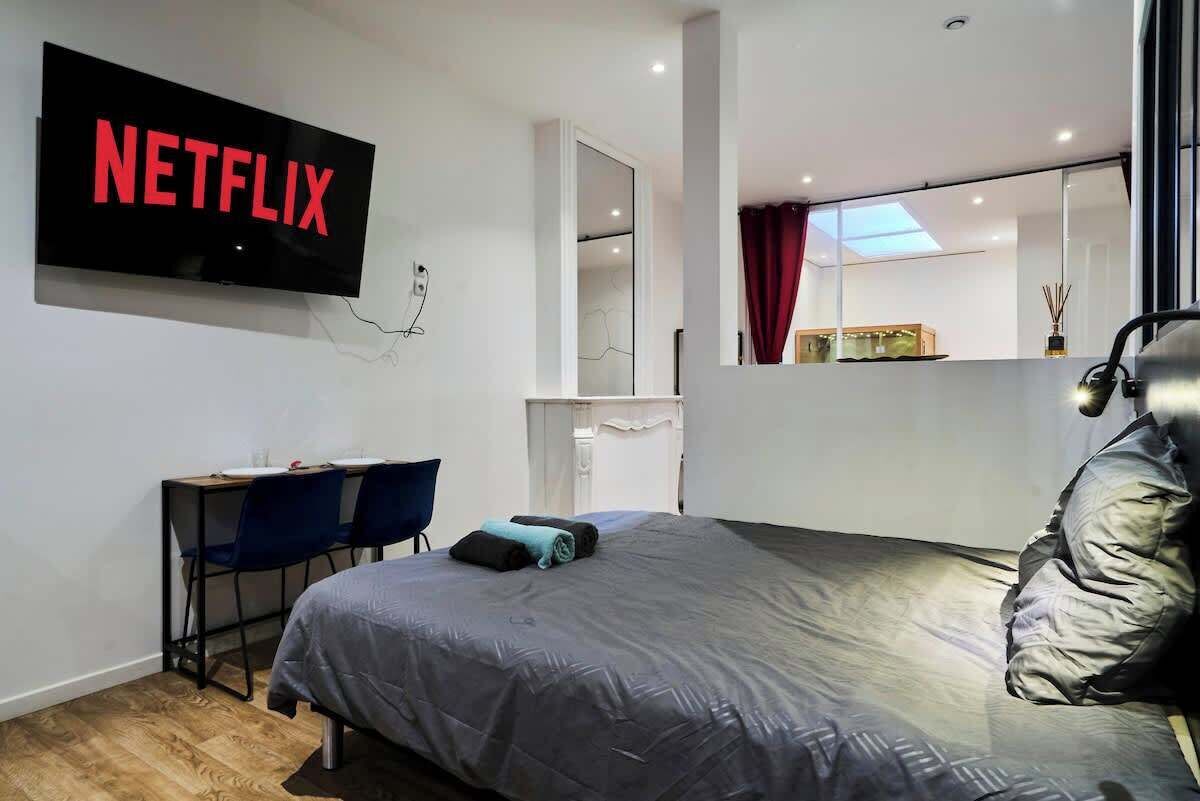 Una habitación de hotel moderna con una cama grande, un escritorio con silla, un televisor montado en la pared y un espejo sobre la cama.