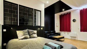 A modern bedroom with a large bed, a black headboard, a leather sofa, and a red curtain. - Baignoire Blanéo & Sauna, 10 minutes de la gare (Tourcoing)