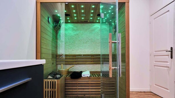 A glass-enclosed sauna with wooden benches, a wooden floor, and a ceiling with recessed lighting. - Baignoire Blanéo & Sauna, 10 minutes de la gare (Tourcoing)