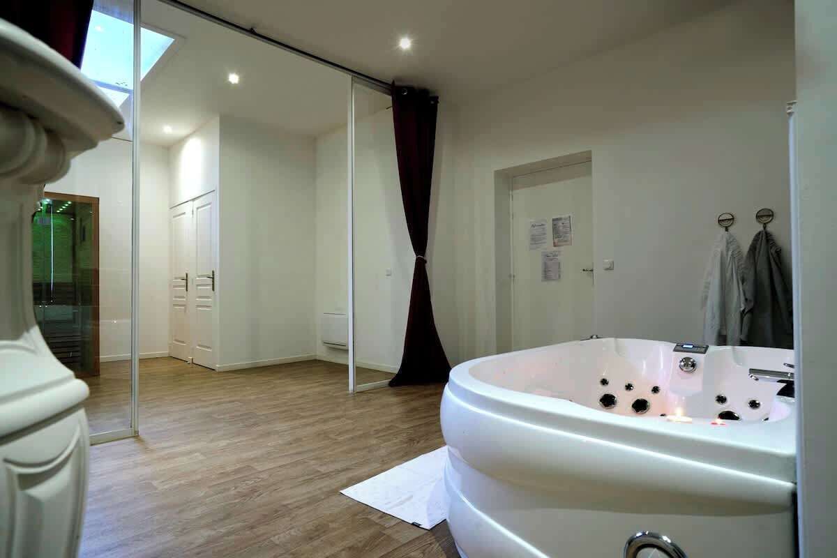 A modern bathroom with a large bathtub, wooden flooring, a sliding glass door leading to a shower area, and a white towel rack.