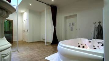 A modern bathroom with a large bathtub, wooden flooring, a sliding glass door leading to a shower area, and a white towel rack.