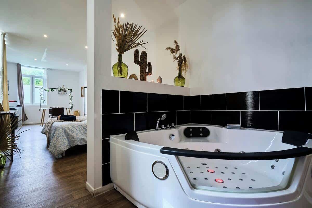 A modern bathroom with a large bathtub, black tiled walls, and decorative plants.