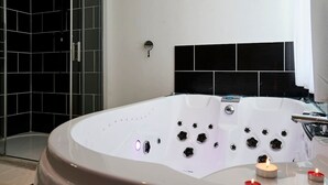 Een moderne badkamer met een groot, wit bad, een douchegedeelte met zwarte tegels en een zwart hoofdeinde.