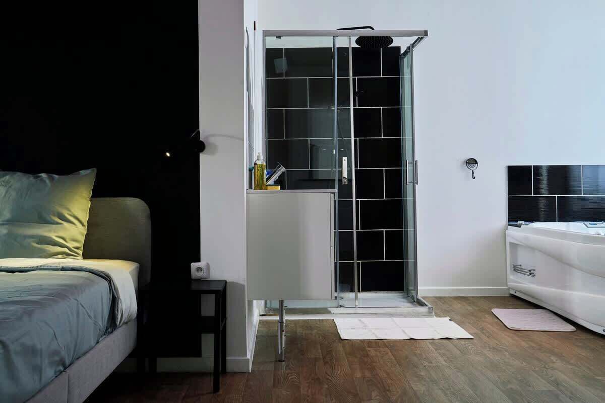 Ein Schlafzimmer mit Bett, Nachttisch, Duschkabine aus Glas und einer weißen Heizung.