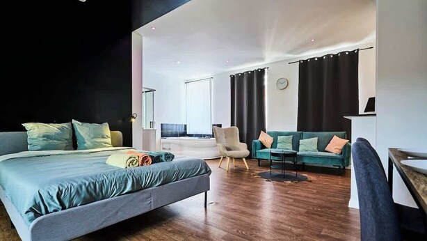 Een moderne hotelkamer met een groot bed, een zithoek met een bank en fauteuils, een eettafel en uitzicht op de stad.