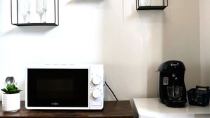 Een kitchenette met een magnetron, een koffiezetapparaat en een kleine potplant op een houten tafel.