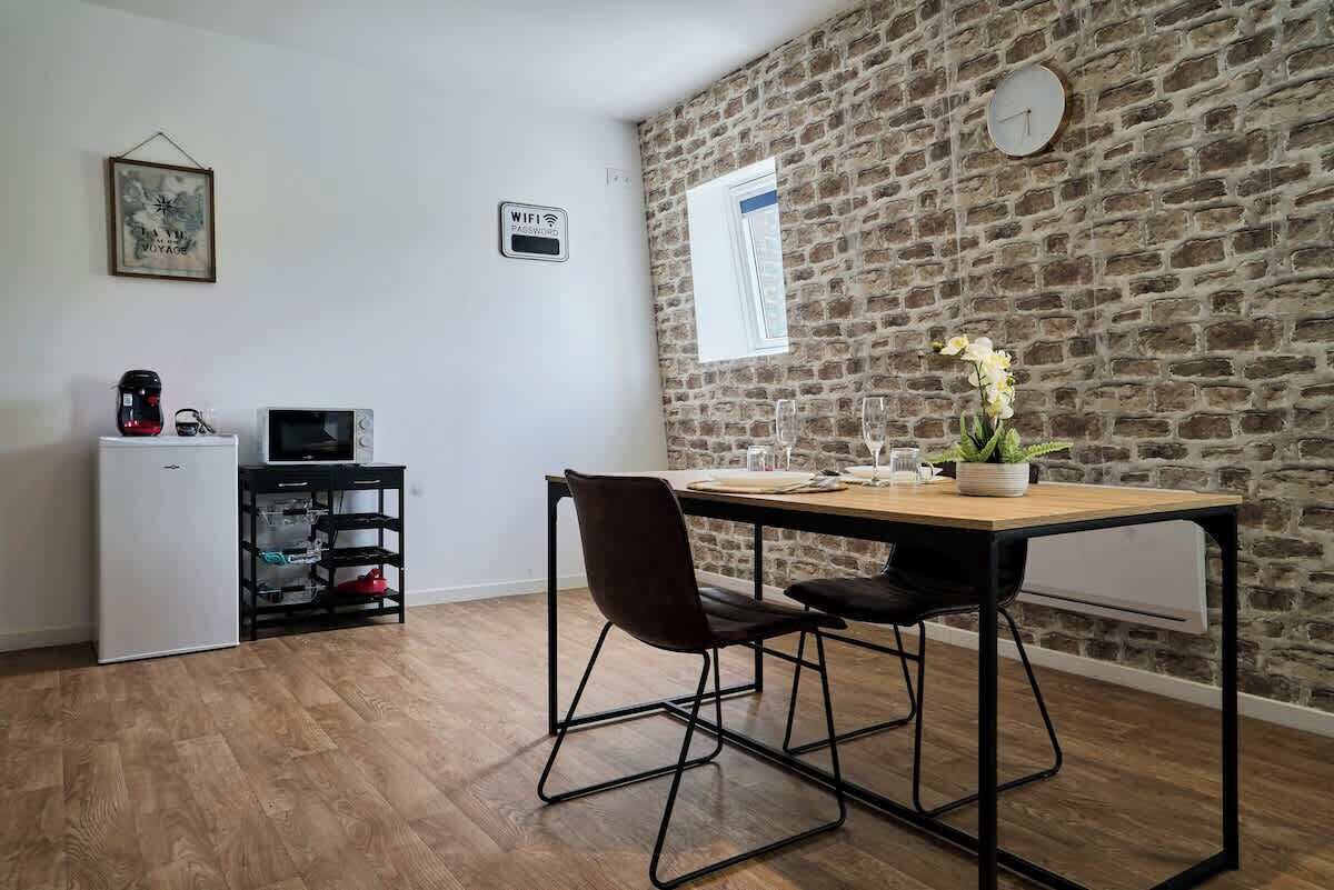 A compact kitchen with a stone wall, a small refrigerator, a microwave, and a dining area with a table and chairs.