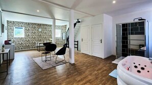Ruime kamer met een stenen muur, houten vloer, zwarte stoel, witte deur en een groot bad.