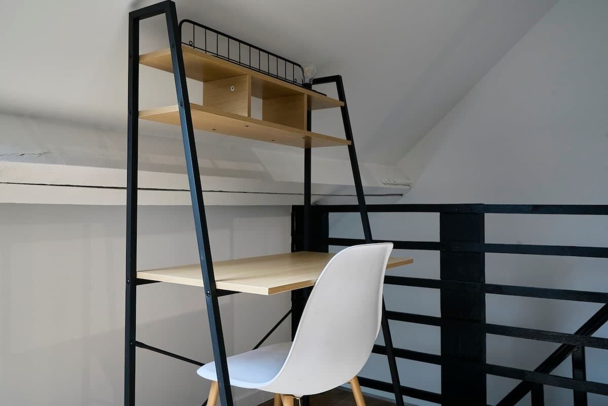 A room with a black metal shelving unit with wooden shelves, a white chair, and a slanted ceiling.