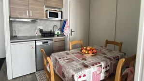 A compact kitchen with wooden cabinets, a microwave, and a dishwasher. A dining table with a checkered tablecloth and a bowl of fruit is in the center. - Apartment les Oursons, 5 persons (La Plagne Tarentaise)