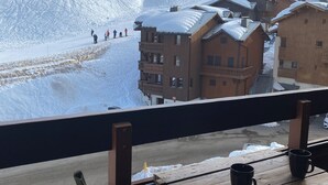 A wooden deck with a table and chairs, overlooking a snow-covered slope with buildings and skiers. - Apartment les Oursons, 5 persons (La Plagne Tarentaise)