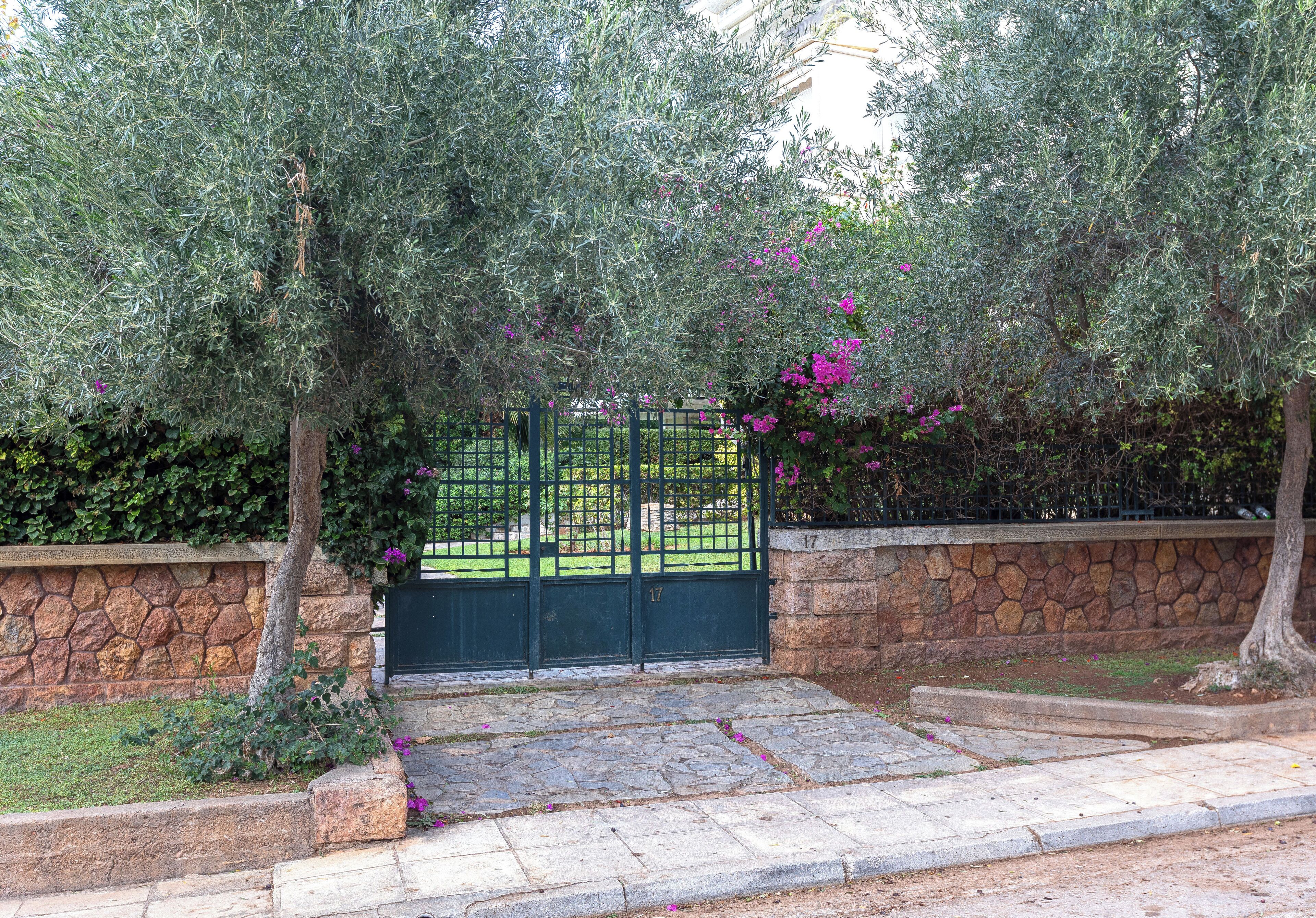 A stone wall, a metal gate, and a paved area with steps leading to a gate.