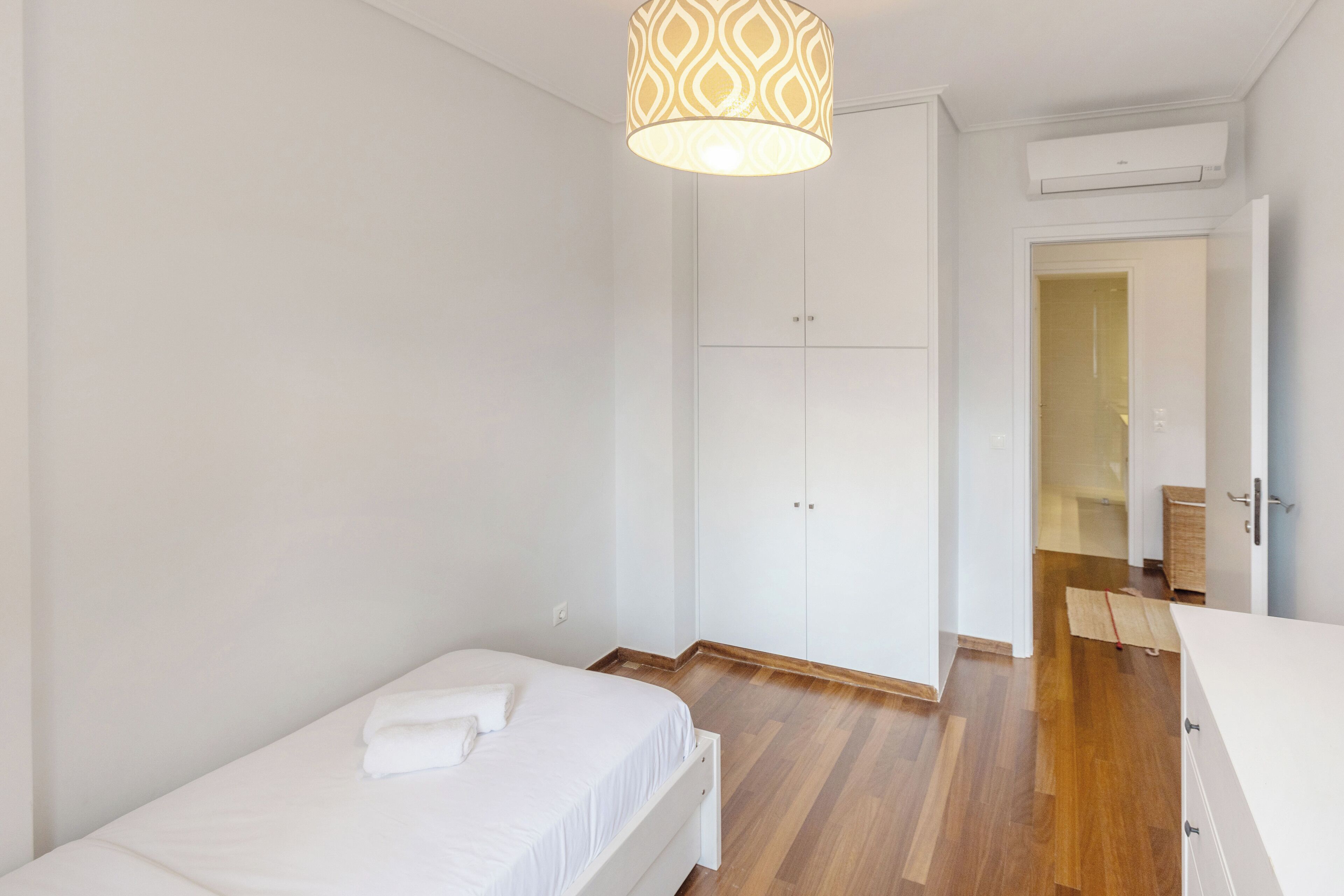 A bedroom with a single bed, a wardrobe, and a hanging light fixture.