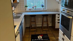 Eine kleine Küche mit Fenster, Spüle, Barhocker und einer Fußmatte.