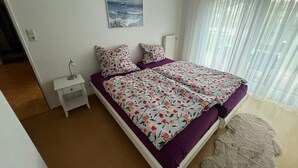 Ein Schlafzimmer mit einem Bett, einem Nachttisch, einem Bild und einem Fenster mit Vorhängen.
