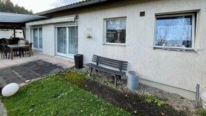 Ein Haus mit einer Terrasse, einem Tisch, einer Bank und einem Mülleimer.