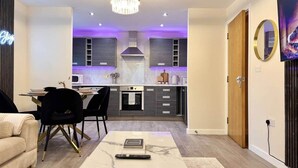 A modern living room with a marble coffee table, a dining area with black chairs, and a kitchen with grey cabinets and a central island. - Modern 4-Bed House • Sleeps 9 •Free Parking, Leeds (Leeds)