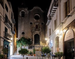 Ένα ιστορικό κτίριο με μια κεντρική, καμάρα στο κεντρικό άνοιγμα της εισόδου, που πλαισιώνεται από μπαλκόνια και γλάστρες με φυτά.