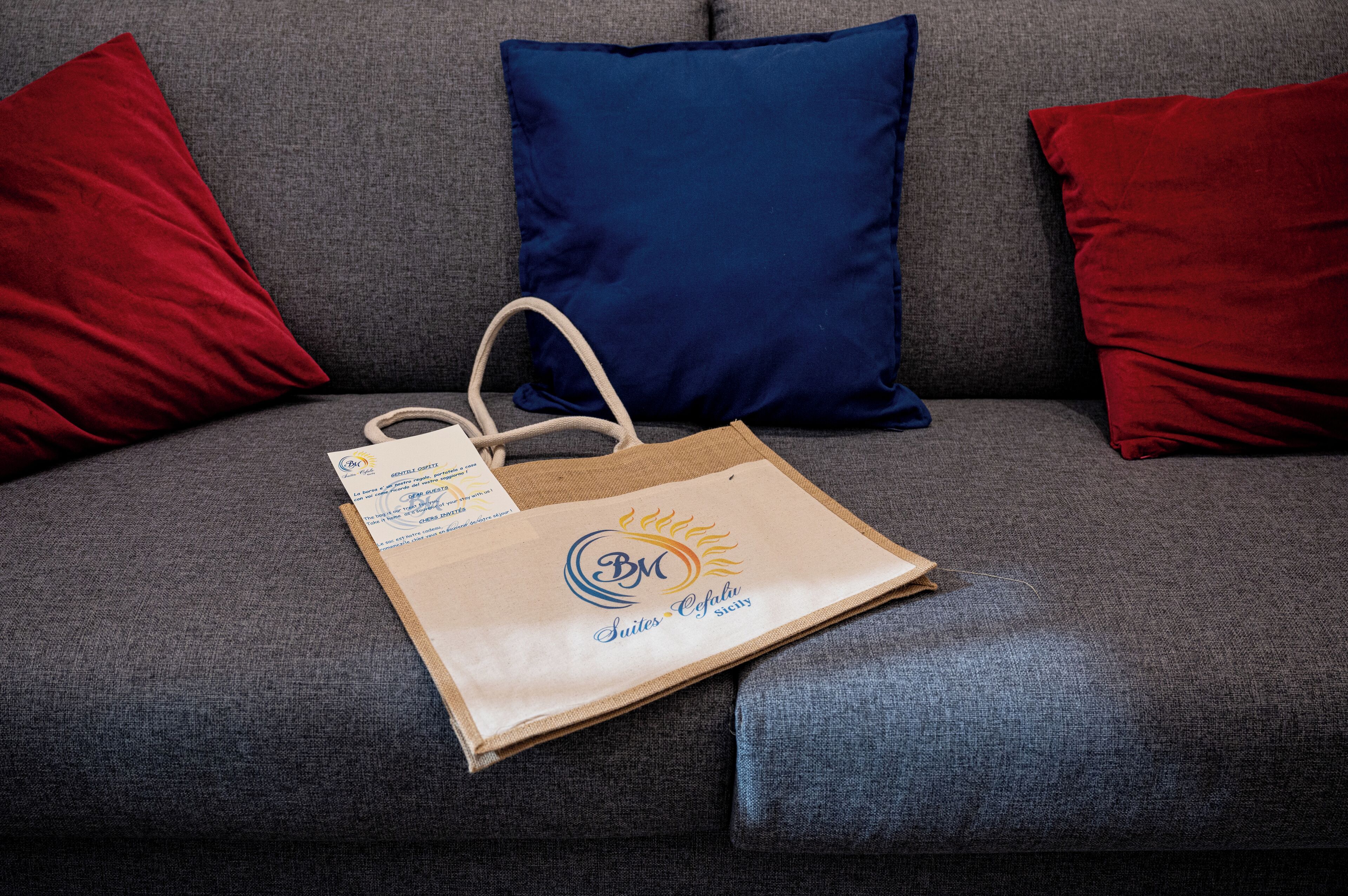 A brown paper bag with a logo and text on a grey sofa with red and blue pillows.