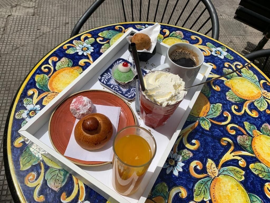 A tray with a pastry, a glass of orange juice, and a cup of coffee on a colorful table.