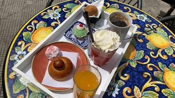 Una bandeja con un pastel, un vaso de jugo de naranja y una taza de café sobre una mesa colorida.