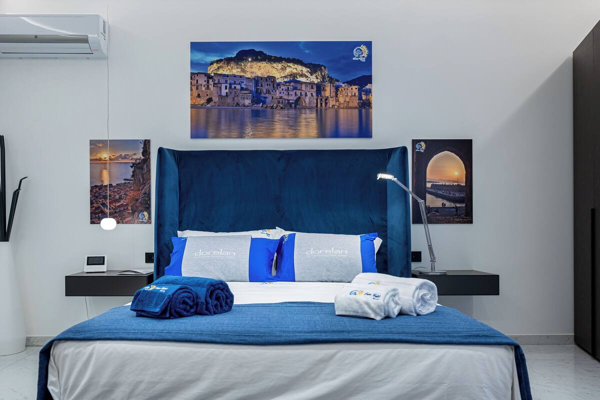 A hotel room with a large bed, a nightstand, a desk, and a wall-mounted air conditioner.