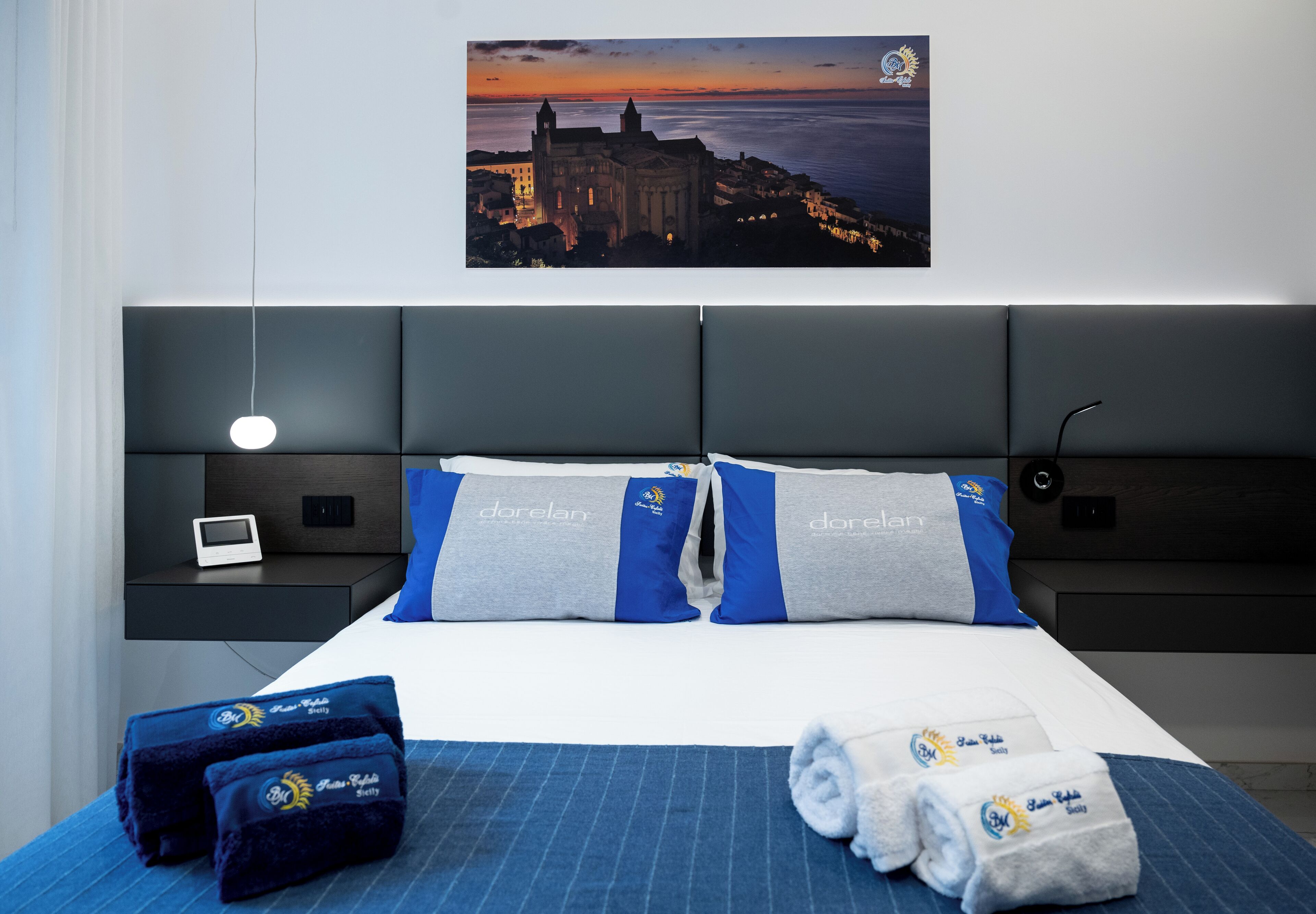 A hotel room with a large bed, two pillows, a nightstand, a wall-mounted picture, and two towels.