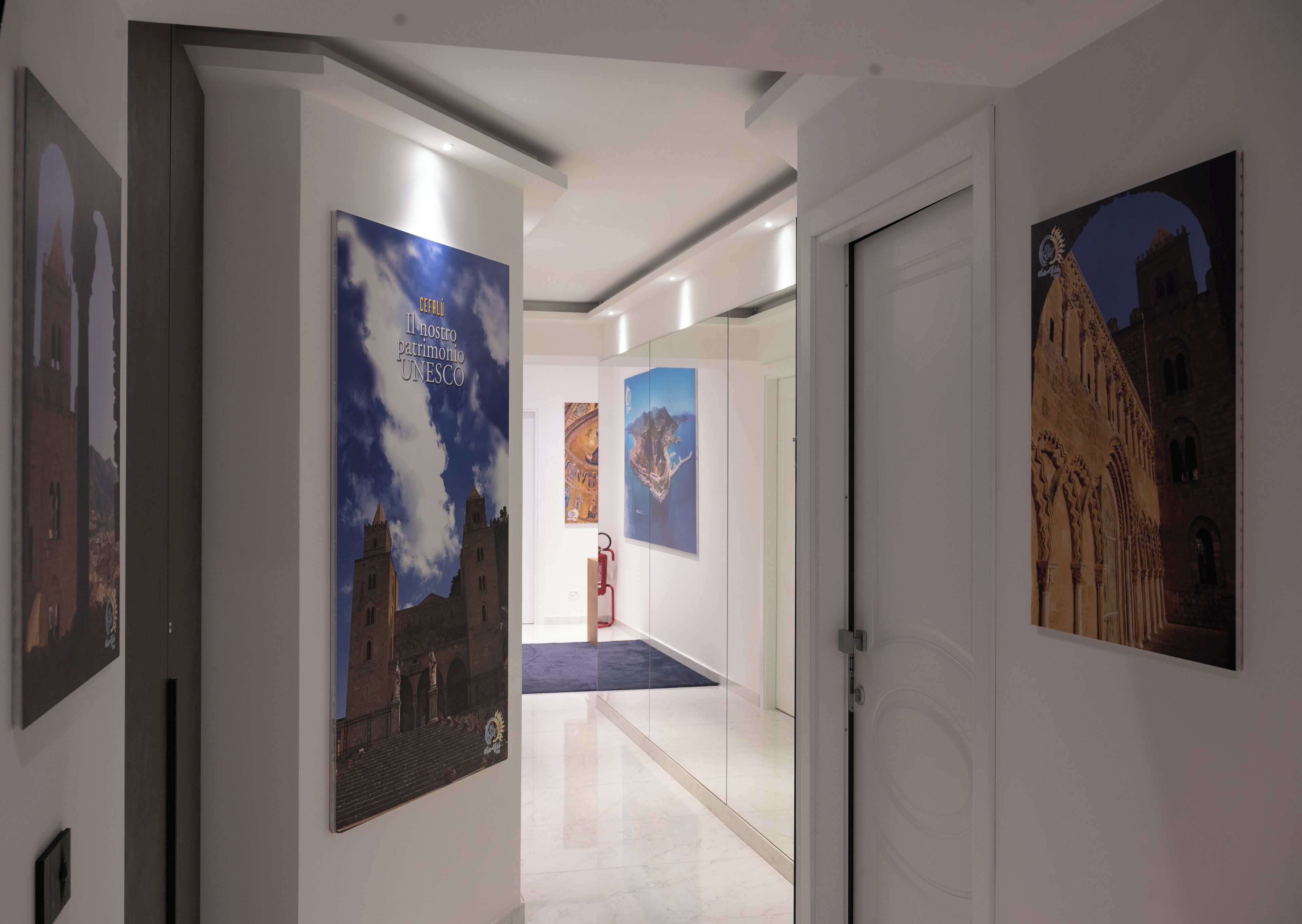 A hallway with white walls, a marble floor, and several framed pictures of buildings.