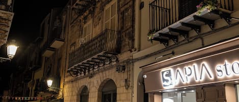 Ein nächtlicher Straßenblick mit einem Boutique-Geschäft namens 'SAPIA STO', das eine Schaufensterpuppe zeigt.