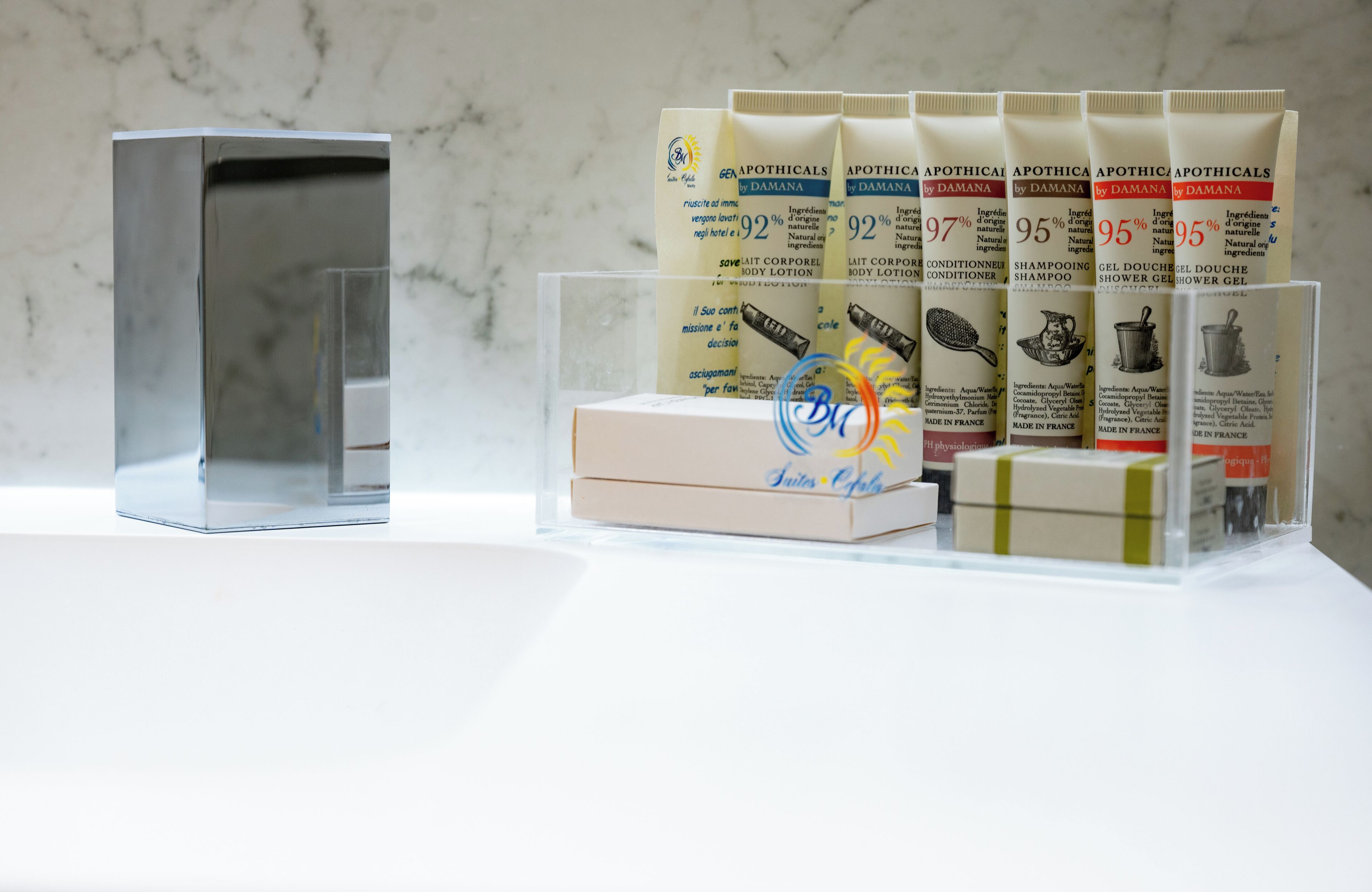 En uppsättning olika hygienprodukter, inklusive kroppslotion, balsam, schampo och duschgel, placerade på en vit yta med en bakgrund i marmor.