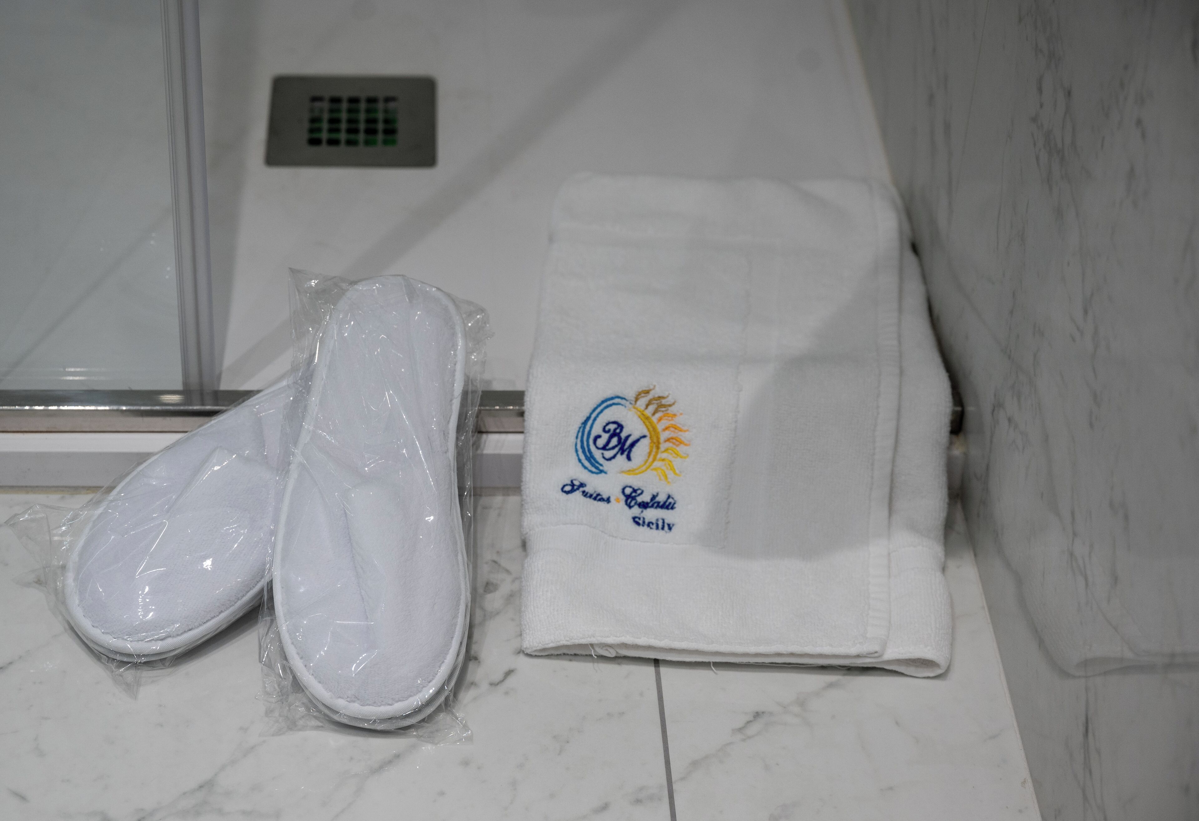 Un baño con una toalla blanca y zapatillas en el suelo, un perchero y un suelo de mármol.