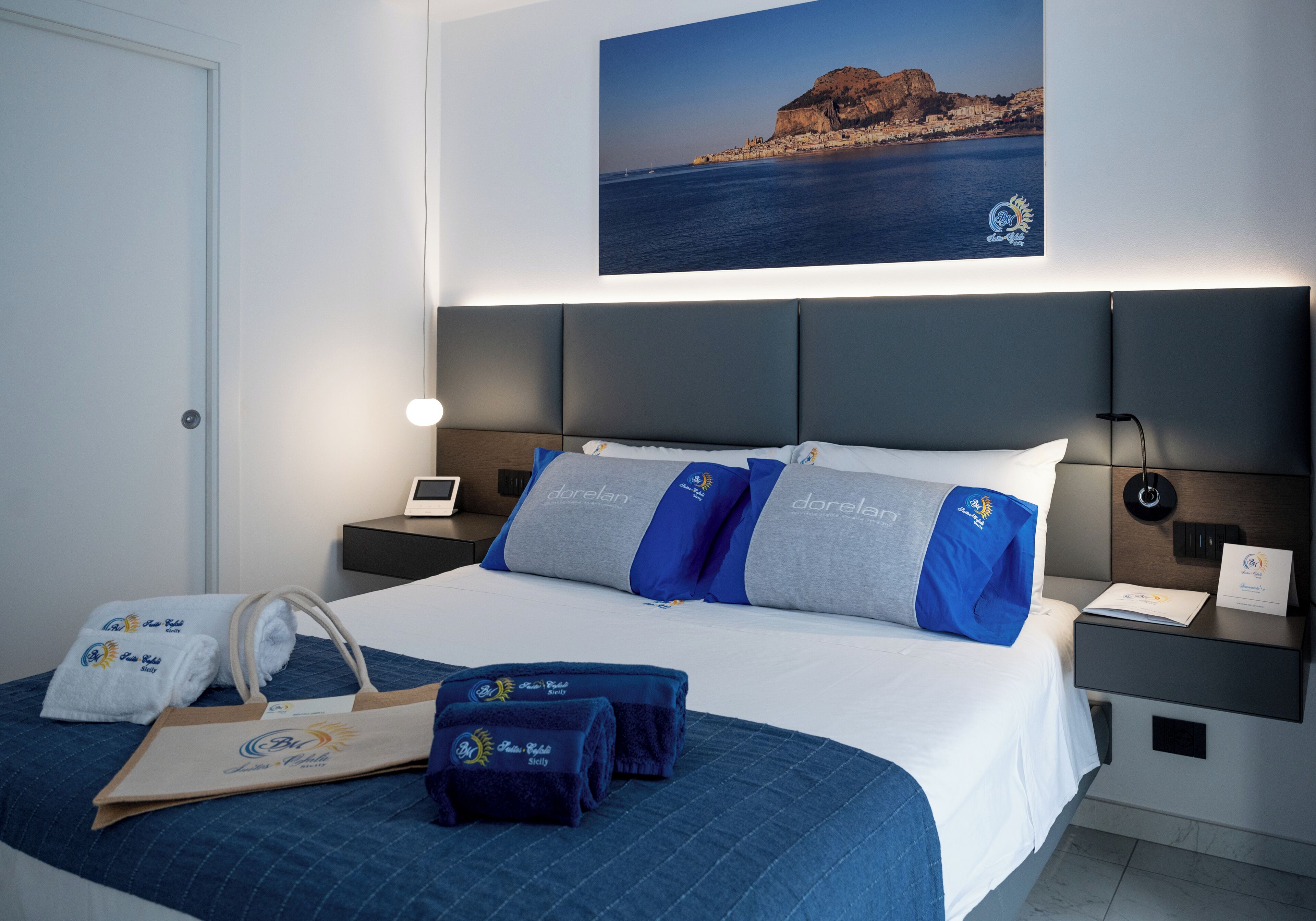 Habitación de hotel con cama, mesita de noche, un cuadro en la pared y una bolsa para toallas.