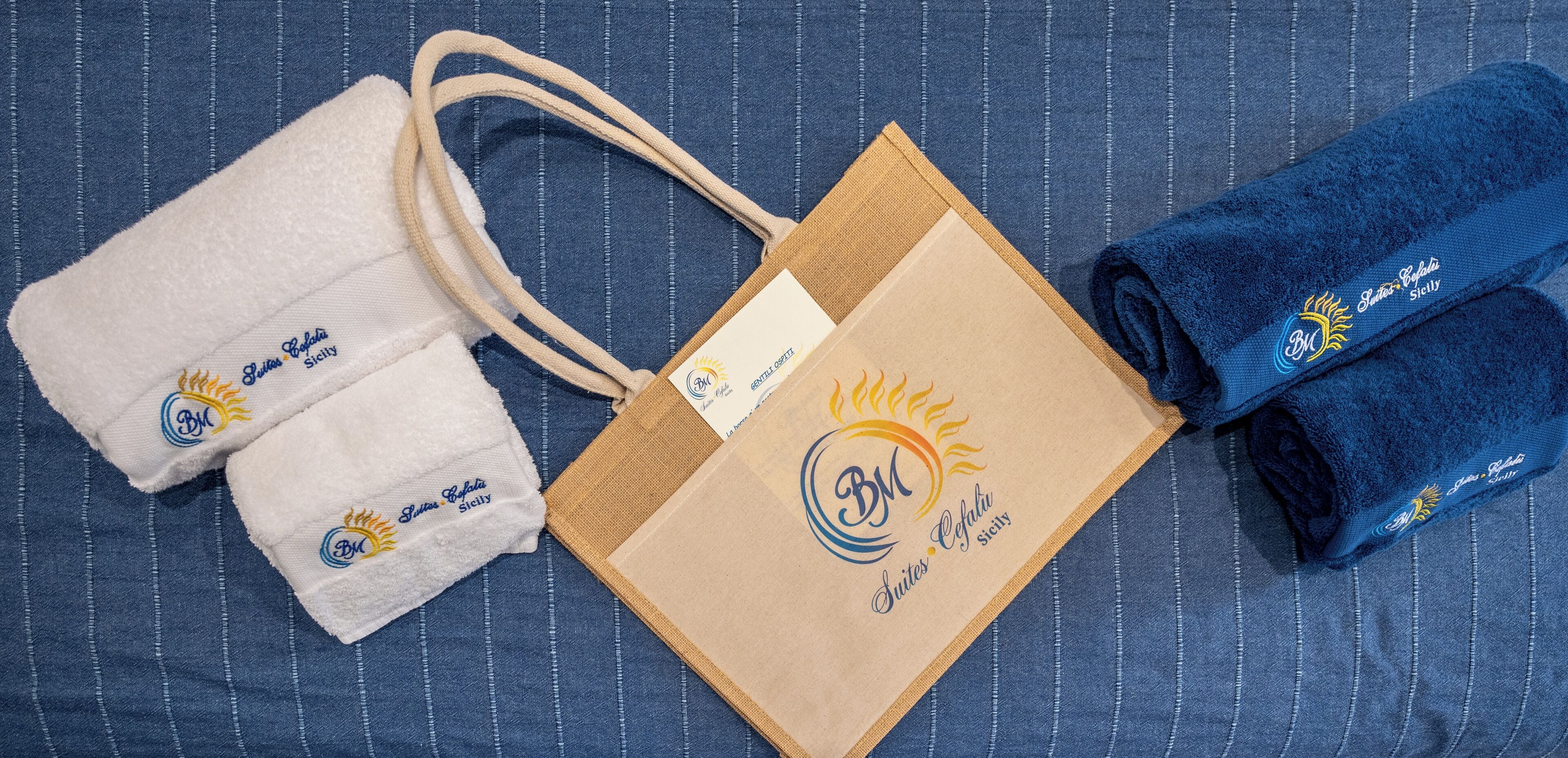 A set of towels, a brown paper bag, and a blue towel with a logo on a blue striped fabric background.