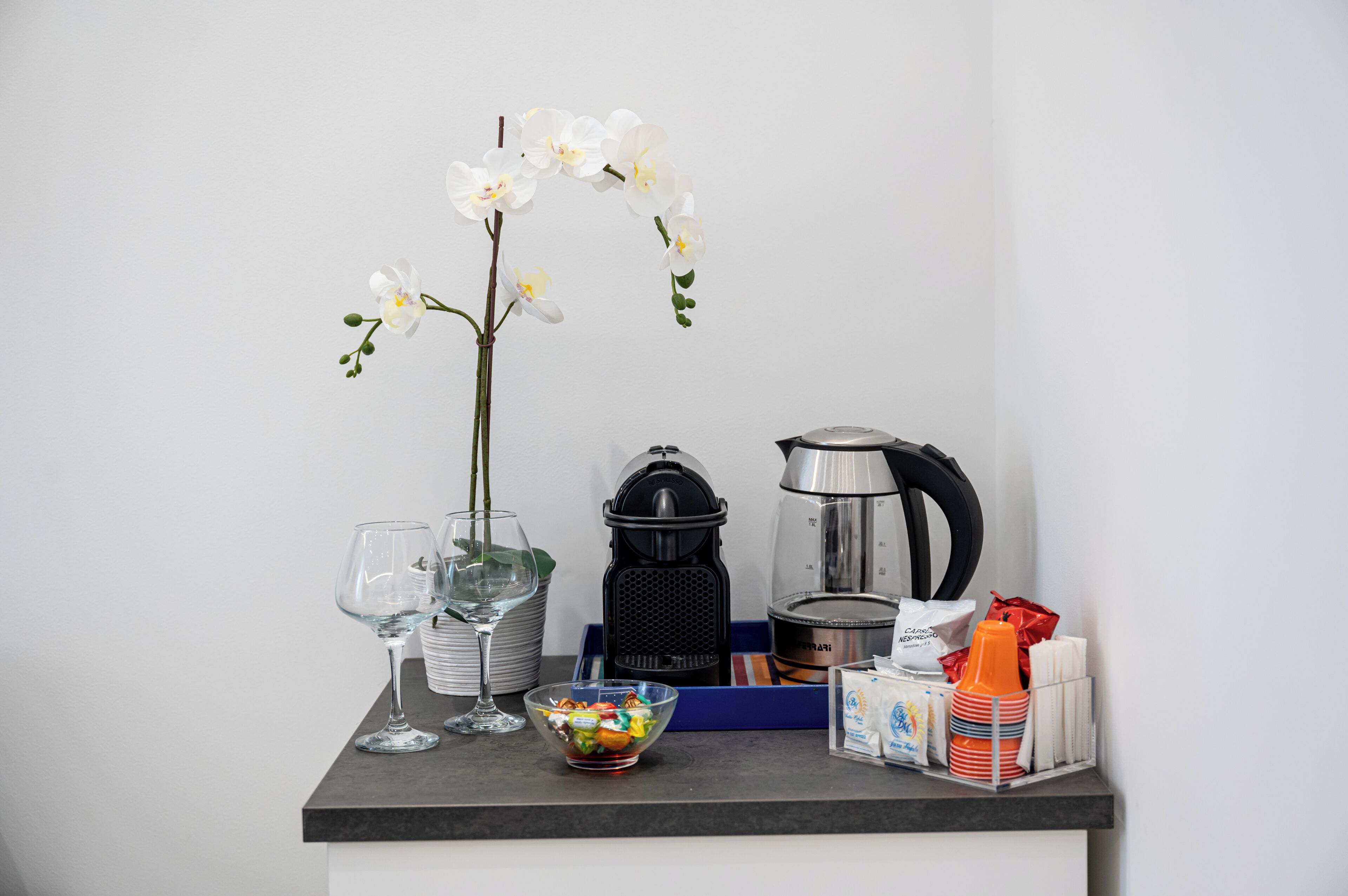 A kitchen counter with a coffee maker, a kettle, a bowl of snacks, and a vase with white flowers.