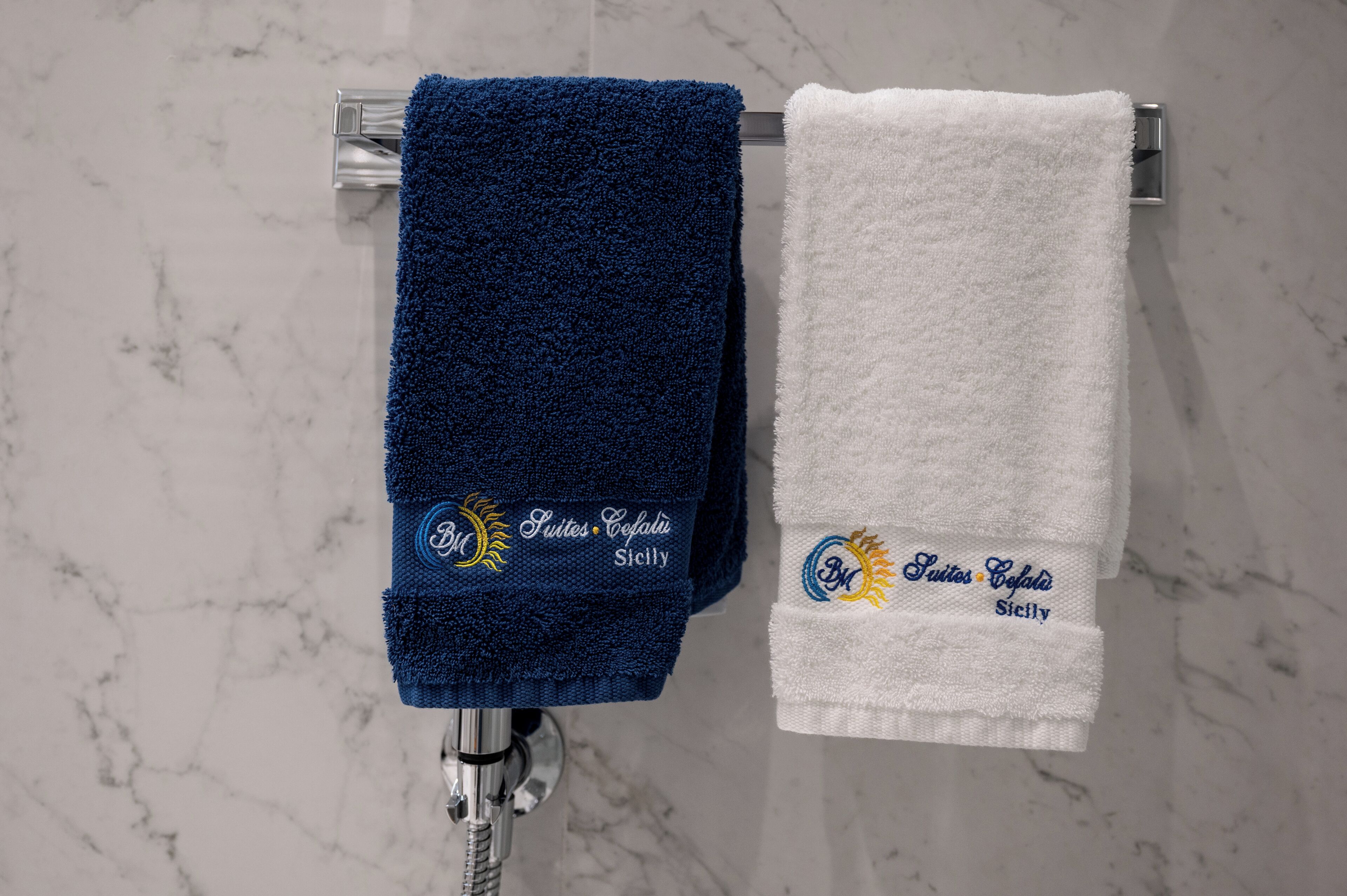 Two towels hanging on a rack, one blue and one white, with embroidered text.