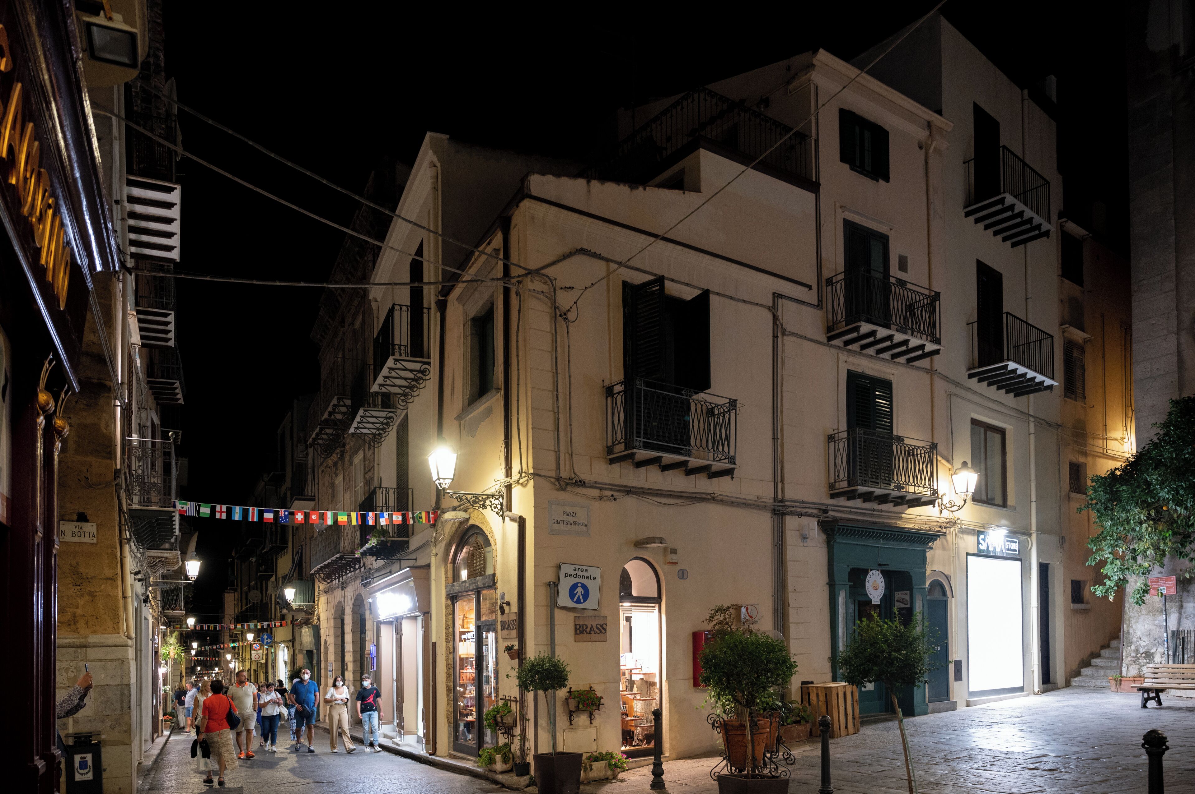 A narrow street with buildings on either side, some with balconies and signage indicating shops or businesses.