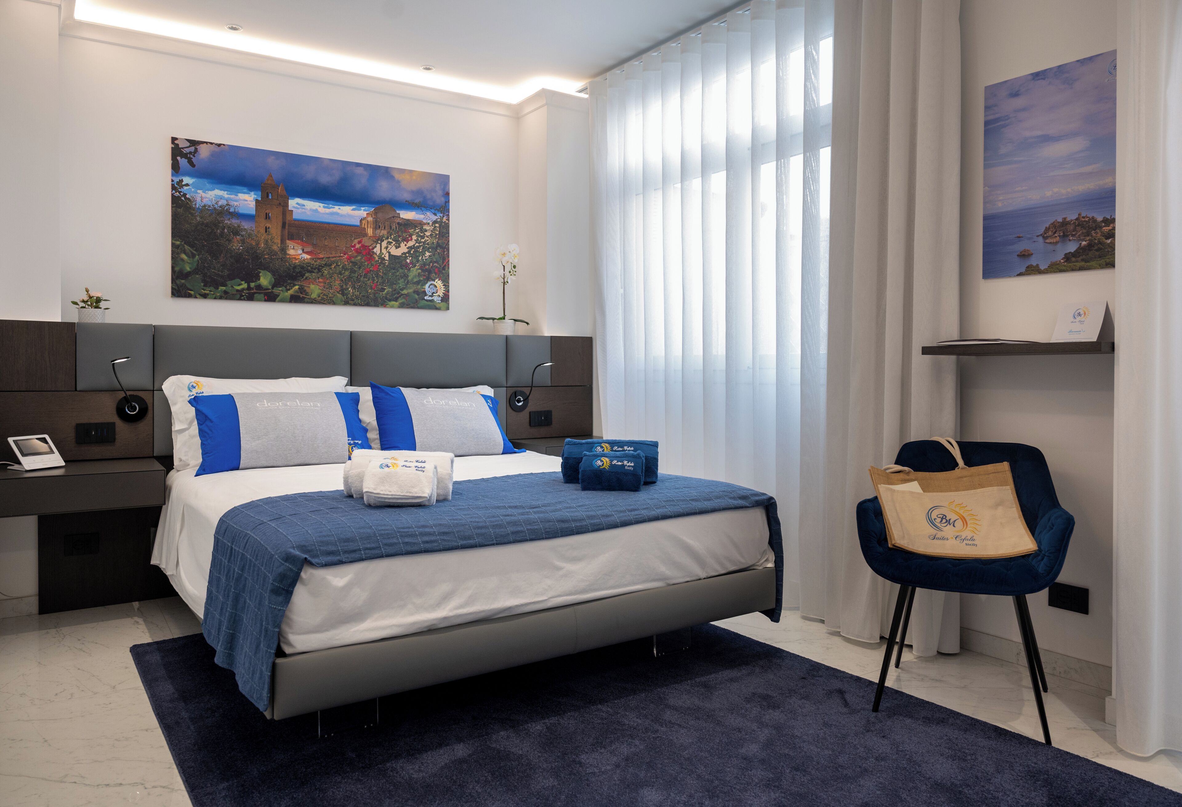 Quarto de hotel moderno com uma cama grande, uma mesa de cabeceira com telefone, uma cadeira e um quadro na parede.