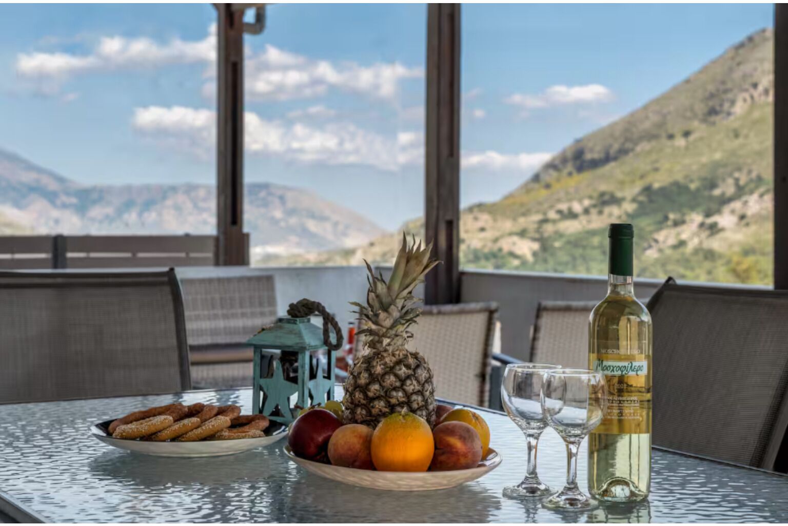 Una mesa con una botella de vino, un plato de fruta y pasteles, con una montaña al fondo.