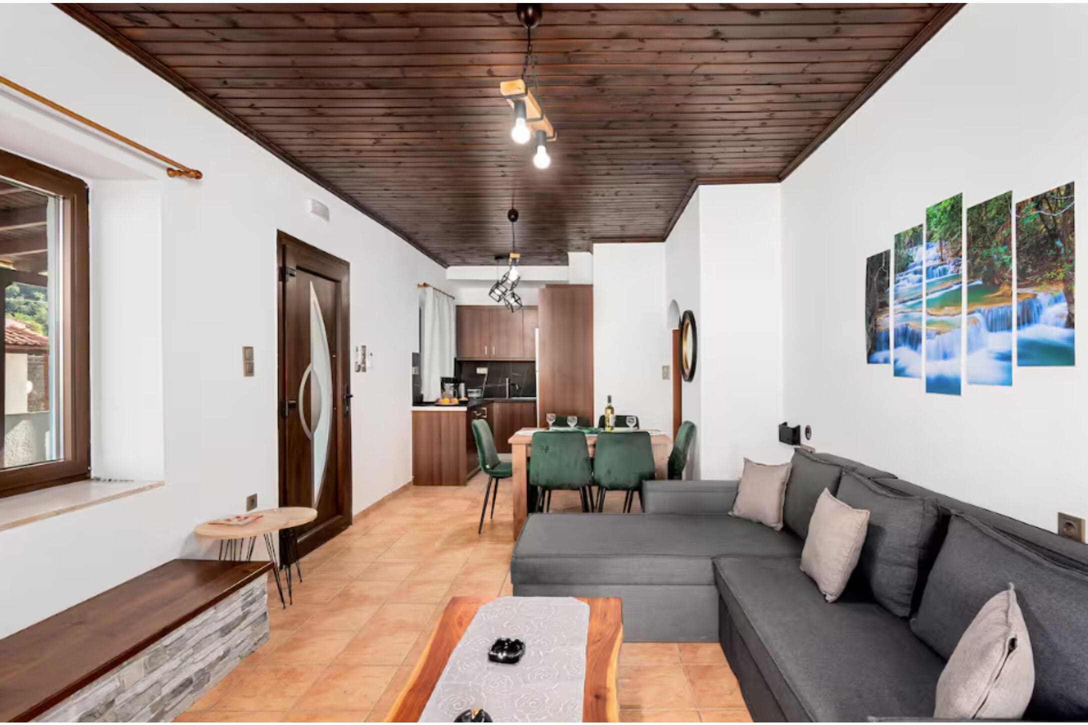 A modern living room with a gray sofa, a wooden coffee table, and a dining area with green chairs.