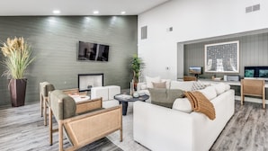 A modern living room with a sofa, chairs, a coffee table, and a TV. There is a plant and a fireplace. - Modern North Austin Retreat by The Domain (Austin)