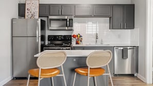 A modern kitchen with grey cabinets, stainless steel appliances, a white countertop, and two wicker chairs. - Modern North Austin Retreat by The Domain (Austin)