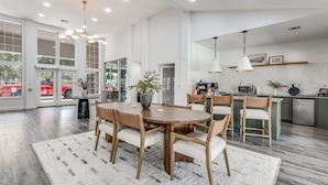 A spacious dining area with a wooden table and chairs, a large rug, and a view of the kitchen in the background. - Modern North Austin Retreat by The Domain (Austin)