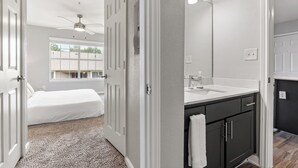 A bedroom with a bed, a bathroom with a sink and mirror, and a hallway with a ceiling fan. - Modern North Austin Retreat by The Domain (Austin)