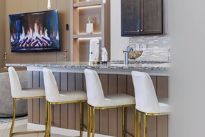 A modern kitchen with a bar area, a flat-screen TV, and a decorative backsplash. - 10BR house at Windsor Cay Resort (Clermont)